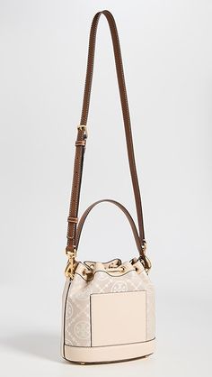 Find TORY BURCH T Monogram Bucket Bag on Editorialist. This Tory Burch bucket bag features a structured silhouette with gold-tone hardware. The bag is crafted from jacquard with a monogram pattern and leather trim. It has a drawstring top, patch interior pocket, and an optional adjustable strap. The bag is lined in suede and has a height of 8.25 inches, a length of 8.25 inches, and a depth of 4.75 inches. The strap drop is 21.75 inches and the handle drop is 4 inches. Monogram Canvas Pouch Shoulder Bag With Gold-tone Hardware, Monogram Canvas Bucket Bag With Detachable Handle, Gold Monogram Canvas Shoulder Bag With Double Handle, Everyday Bucket Bag In Monogram Canvas With Gold-tone Hardware, Everyday Monogram Canvas Bucket Bag With Gold-tone Hardware, Monogram Canvas Bucket Bag With Gold-tone Hardware, Gold Bucket Bag With Top Handle And Gold-tone Hardware, Luxury Bag In Monogram Canvas With Brass Hardware, Gold Monogram Canvas Shoulder Bag With Dust Bag