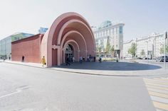 an empty street in front of a building with arches on the sides and people standing outside