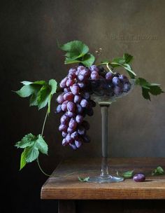 a glass filled with grapes sitting on top of a wooden table