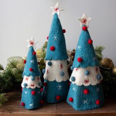 three blue christmas trees with red and white decorations on them, sitting on a wooden table