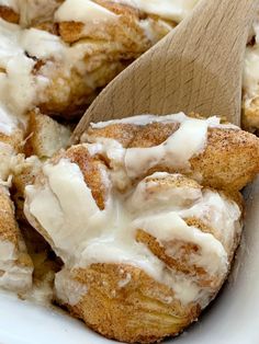 cinnamon rolls with icing and a wooden spoon in a white dish on a table