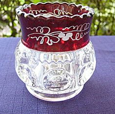 a red glass vase sitting on top of a purple table cloth next to a tree