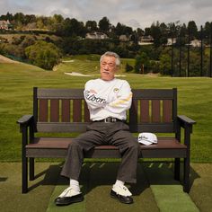 an older man sitting on a bench in the grass with his arms crossed and feet crossed