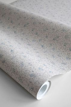 a white and blue wallpaper with small flowers on the side, next to a roll of paper