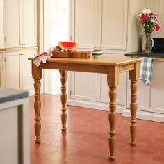 a wooden table sitting in the middle of a kitchen next to a vase with flowers