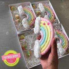 a hand holding a rainbow shaped cake in a box with white frosting on it