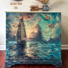 a painted dresser with a sailboat in the ocean on it's sideboard