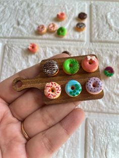 a hand holding a miniature wooden tray with different donuts on it's sides