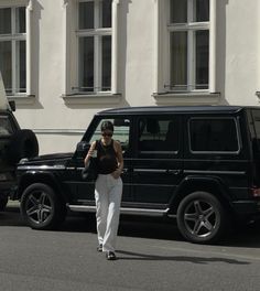 a woman walking past a black car in front of a white building