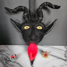 a black mask with yellow eyes and horns on top of a marble table next to other items