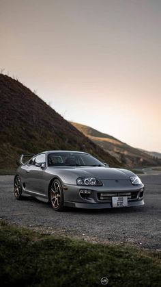 a silver sports car parked on top of a gravel road