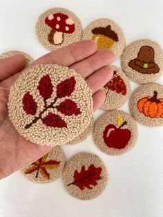 a hand is holding some crocheted coasters with autumn designs on them,