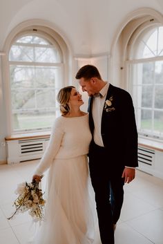 a bride and groom standing together in front of large windows