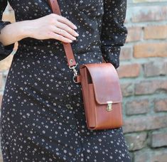 a woman wearing a black dress and holding a brown leather handbag on her shoulder