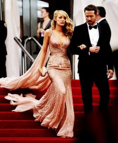 a man in a tuxedo and a woman in a gown walking down the stairs