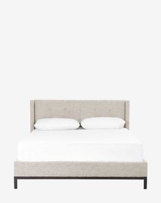 a bed with two pillows on top of it and a white wall in the background