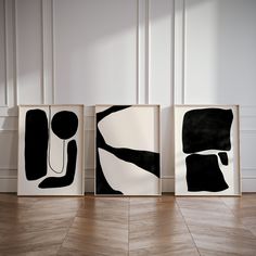 three black and white abstract paintings on the wall in front of a wood paneled floor