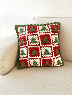 a crocheted christmas pillow sitting on top of a white couch next to a wall