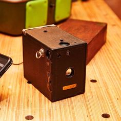 an old camera sitting on top of a wooden table next to a cell phone and another device