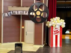 a movie reel and some balloons in front of a red carpeted room with curtains