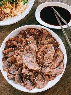 two plates of food on a table with chopsticks and sauce in the bowl