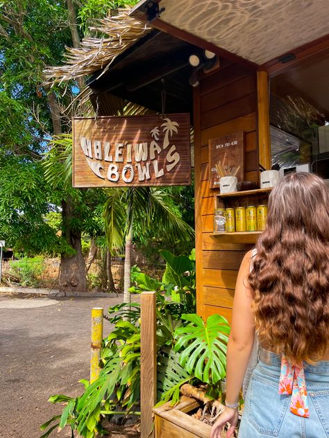 wooden Haleiwa Bowls shack surrounded by bright green leaves and a woman standing to the right ordering a smoothie North Shore Aesthetic, Hawaii College Aesthetic, College In Hawaii, Living In Hawaii Aesthetic, Oahu Aesthetic, Lihue Hawaii, North Shore Hawaii, Hawaii Aesthetic, Hawaii House