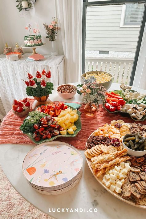 Looking for fairy-themed party food ideas for your kid's birthday? Look no further! Create an enchanting garden table with strawberry mushrooms, fruit platters, veggie platters with hummus/dip, a cheese and cracker board, salads, and cheese sliders. Don't forget the chips, pretzels, and applesauce pouches. And of course, there's a magical theme cake for dessert too. Get inspired by reading our blog post! Lucky Andi. Fairy Birthday Party: Food Ideas Cheap Birthday Party Food Ideas, Fairy Garden Snacks, Fairy Birthday Party Snacks, Food To Serve At 1st Birthday Party, Fairy Party Food Ideas For Kids, Fairy Birthday Food Table, Woodland Fairy Birthday Party Food, Fairy Party Menu Ideas, Fairy First Food Ideas