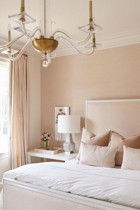 A brass and acrylic chandelier illuminates a blush pink bedroom featuring blush pink velvet pillows place don a blush pink bed positioned against a blush pink wall. Bedroom Pillows Arrangement, Blue Upholstered Bed, White Wooden Bed, Blush Pink Bedroom, Blush Bedroom, Pink Headboard, Restful Bedrooms, House Interior Design Styles, Transitional Bedroom