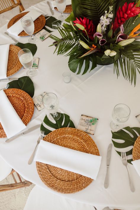 Elegant tropical reception decorations for your beach wedding. The reception table is decorated with a rattan charger, white table cloth, a white napkin, a monstera leaf and a tropical centerpiece. Save for inspiration. Boho Tropical Wedding Table Decor, Beach Wedding Reception Table Decor, Tropical Place Cards, Minimal Tropical Centerpiece, Monstera Leaf Table Decor, Tropical Table Decor Wedding, Tropical Centerpieces Wedding Receptions, Beach Wedding Reception Ideas Table Decorations, Tropical Garden Wedding Decor