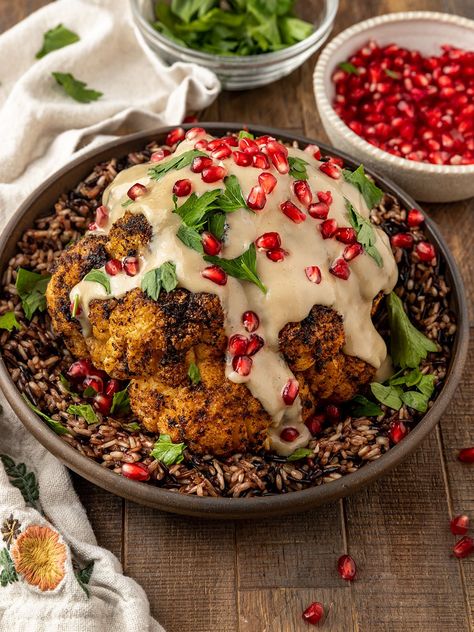 This vegan & gluten-free Whole Roasted Cauliflower topped with a maple tahini sauce, fresh pomegranate, & parsley is a show-stopper main dish for the Holidays. This vegan cauliflower roast is made in a dutch oven for an easy Thanksgiving or Christmas main dish. The best vegan roasted cauliflower recipe! Baked Cauliflower Recipe, Christmas Main Dishes, Vegan Christmas Dinner, Roasted Cauliflower Recipes, Whole Roasted Cauliflower, Vegan Roast, Vegan Cauliflower, Vegetarian Main Dishes, Baked Cauliflower