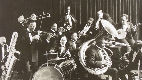 We see a band with some well-known instruments like drums and trombone. They make music that is called Jazz. It became very popular around the 1920s. The men wear neat suits. In the 1920s there were a lot of clubs, lounges and theaters in Chicago which played Jazz music, it was the new trend. It is believed that Jazz made its way through Chicago from New Orleans in 1915. Jazz is a mix of African and European musical traditions that started in the United States by african migrants form the west. 1920s Jazz, Violin Accessories, Chicago History Museum, Electric Violin, Popular Bands, Jazz Artists, Jazz Band, Jazz Club, Jazz Age