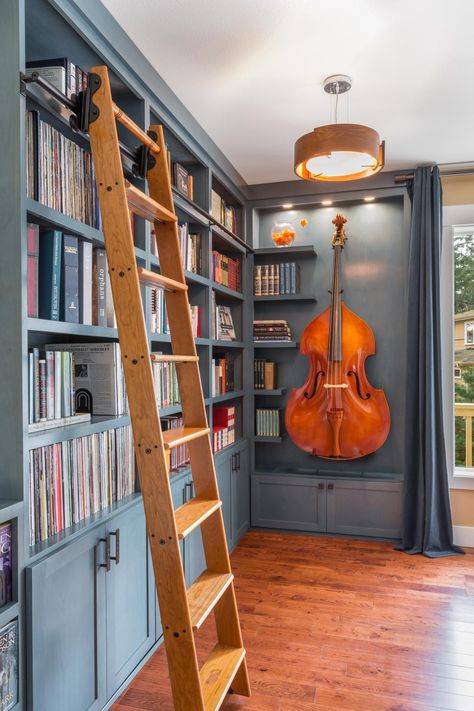 HGTV presents a gorgeous blue home library that once was merely an unused corner in the great room but now serves to display an extensive book and music collection as well as a cello. Home Instrument Storage, Corner Library Shelves, Library In Office Space, Music Collection Room, Bookcase Wall With Ladder, Bookshelf Wall With Ladder, Coastal Home Library, Library Room With Ladder, Library With Ladder Book Wall