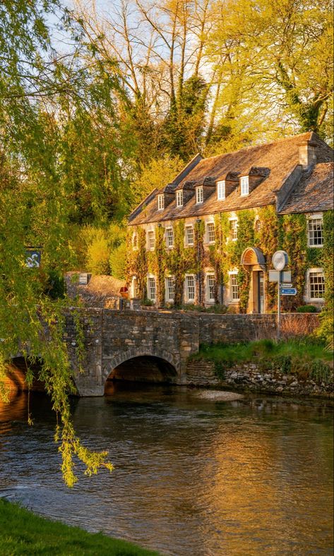 A period property in the evening sunshine behind a river and small road bridge. The spring scene is surrounded by trees that are beginning to bloom. England Aesthetic, Cotswolds England, England Countryside, Castle Combe, Voyage Europe, Dream Travel Destinations, The Cotswolds, English Countryside, England Travel