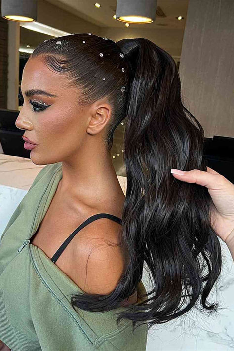 Image of a wavy ponytail upstyle adorned with hair gems, perfect for adding glamour to summer nights. Coldplay, Long Ponytails Hairstyles, Slick Back Ponytail With Gems, Slick Back With Gems, Upstyle Ponytail Hairstyles, Glitz And Glam Hairstyles, Ponytail With Gems, Hair Styles With Gems, Hoco Hair Ponytail