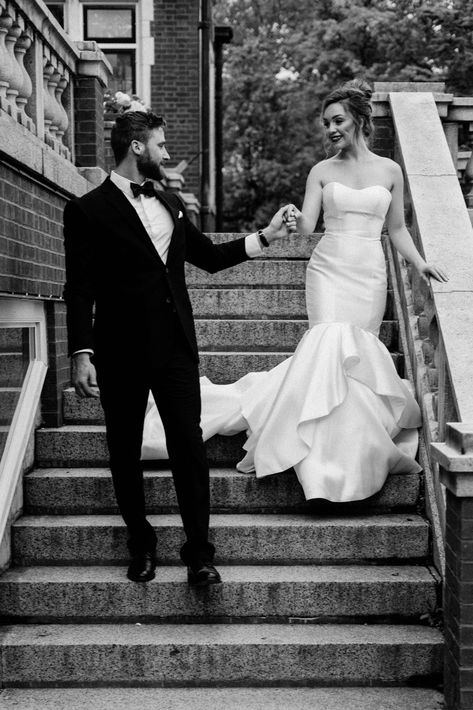 Classic black and white of couple on a wedding day walking down the stairs at Glensheen Mansion in Duluth, MN. Groom is wearing a classic black tux and bride is in a stunning satin mermaid gown by Allure bride. Wedding Photoshoot Elegant, Wedding Stair Poses, Wedding Couple Poses On Stairs, Black And White Wedding Photoshoot, Wedding Photography On Stairs, Bride Stairs Photography, Wedding Poses Stairs, White Gown Couple Photoshoot, Bride And Groom Staircase Photos