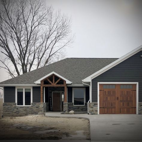 Stone Siding Exterior Ranch Style, Black Metal Roof Dark Grey Siding, Gray House With Rock Exterior, Farmhouse Exterior Ideas Stone, Tan House With White Windows, Navy House With Wood Accents, Dark Grey Siding With Stone, Stone Exterior Ranch Style Home, Wainscoting Exterior House