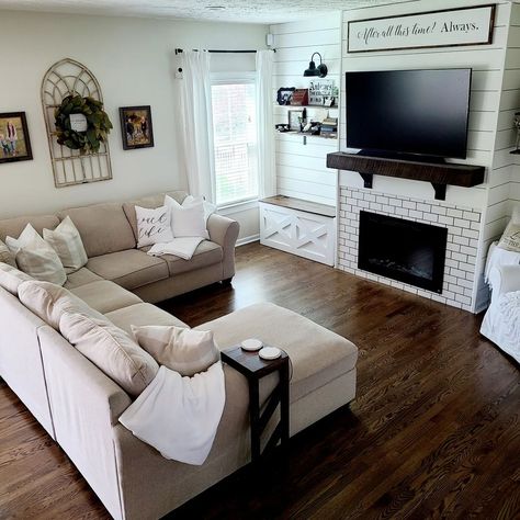 This beige chaise lounge sectional is seated on gorgeous dark wood living room flooring. The sectional faces a white subway tile fireplace fitted into a white shiplap wall. Complement the dark floors with a dark wood mantel mounted above the fireplace. Sofas For Dark Floors, Dark Wood Floor White Walls Living Room, Living Room Furniture With Dark Floors, Boho Living Room With Dark Floors, Modern Living Room With Dark Wood Floors, Wood Floor Furniture Living Rooms, White Living Room Dark Floors, Living Room Paint Color Ideas Dark Floor, Living Room Ideas With Dark Floors