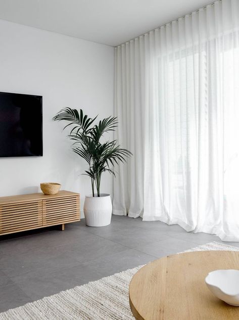 Dark and dull grey living area transformed into a warm and inviting space. The white linen sher curtains, oak side table, seagrass pouf, soft ivory rug, oak entertainment unit and indoor palm tree balance the cold of the grey floor tiles. Click now to see more photos of this beautiful living room Grey Tiles Living Room, Grey Flooring Living Room, Sheers Curtains Living Room, Lounge Room Styling, Tiles Living Room, Living Room Tiles, Living Room Decor Curtains, Room Tiles, Curtains Living