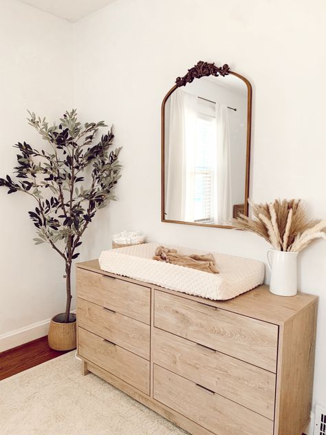 Olive tree with brass mirror. Simple changing table for nursery. Ivory and white. All Natural Wood Nursery, Ikea Natural Wood Dresser, Nursery Natural Wood Dresser, Neutral Nursery Minimalist, Neutral Changing Table, Nursery Ideas Bookshelf, Neutral Nursery Furniture, Neutral Nursery Changing Tables, Natural Dresser Nursery