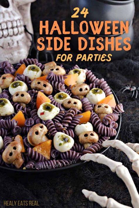 A plate of Halloween-themed pasta containing rotini, mozzarella balls with pesto, and orange bell pepper pieces, garnished to look like skulls; background features a skull and skeleton hand. Text reads "24 Spooky Halloween Side Dishes for Parties." Easy Halloween Main Dishes, Spider Bread Bowls For Halloween, Halloween Cookout Food, Halloween Party Sliders, Spooky One Birthday Food Ideas, Halloween Food Platter Ideas, Spooky Sides For Halloween, Halloween Dinner Sides Ideas, Halloween Food Ideas For Work Party