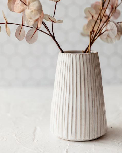 Our tall fluted vase is great for a large bunch of flowers, its textural design adds visual interest while still creating the perfect neutral backdrop to your flower arrangement.It is wheelthrown using Stoneware clay, then handcarved and glazed in white.It measures approx 17.5 cm high x 8.5 cm at t Clay Flower Pots Diy, White Pottery Vase, Tall Pottery Vases, Ceramic Pottery Vase Ideas, Cute Pottery Vase, Beginner Pottery Vase, Textured Ceramic Vase, Vase Clay Ideas, Handmade Ceramic Vase Ideas