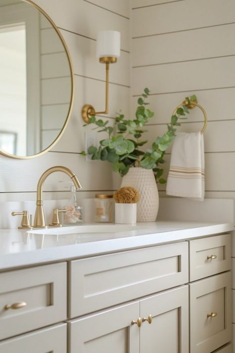 Bathroom sink with gold fixtures, clean countertop, round mirror, wall lamp, eucalyptus in a vase, and a hand towel. Hall Bath Decor, Neutral Home Inspiration, Beige Bathroom Vanity Cabinets, Beige Bathroom Color Schemes, Natural Wood Bathroom Ideas, Spa Like Bathroom Colors, Beige And Gold Bathroom, Neutral Bathroom Vanity, Bathroom Neutrals