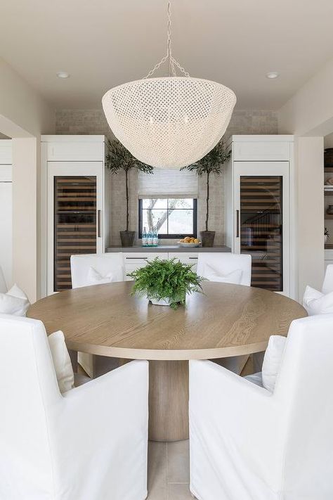 A white basket chandelier illuminates white slipcovered dining chairs placed around a round wood pedestal dining table. Pure Salt Interiors Dining Room, Salt Interiors, Modern Dining Room Ideas, Pure Salt Interiors, Transitional Dining Room, Transitional Dining, Coastal Dining, Pure Salt, Modern Colonial