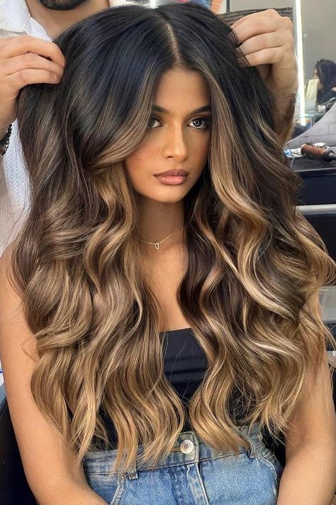 Long voluminous waves with a center part, blending black hair with rich caramel balayage. The cascading curls add depth and movement, enhancing the multi-tonal effect for a glamorous look.  // Photo Credit: Instagram @solotreartofbeauty Caramel Balayage For Black Hair, Caramel Hair Balayage Honey, Dark Brown Hair With Caramel And Blonde Highlights, Caramel Balayage Dark Roots, Dark Long Hair Balayage, Light Caramel Highlights On Black Hair, Black With Caramel Balayage, Baliage Hair Fall, Dark Blonde Balayage Long Hair