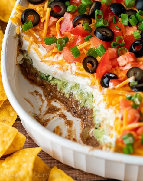 7 Layer Bean Dip with scoop taken out to show layers of beans, guacamole, sour cream and cheese. Spider Web 7 Layer Bean Dip, Black Bean Layer Dip, Halloween Nacho Dip, Easy Birthday Food Ideas, 7 Layer Bean Dip Recipe, Recipe With Refried Beans, Layered Nacho Dip, Layered Bean Dip Recipe, Layered Salads