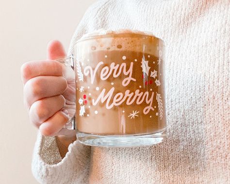 Cozy up by the Christmas tree and enjoy the essence of the holiday season with your favorite festive coffee or hot chocolate! Very Merry Clear Glass mug has a vinyl design hand applied. Festive Christmas mug is the perfect holiday gift!13 oz. clear glass mug with vinyl design applied. Made to order. While the vinyl adhesive is permanent, these mugs are hand wash only. Do not microwave. *Due to the handmade nature of this product, products may vary slightly. Holiday Mugs Diy, Coffee Vinyl Ideas, Clear Coffee Mug Designs, Clear Mug Cricut Ideas, Cricket Vinyl Ideas, Vinyl Christmas Mugs, Christmas Glass Mugs, Christmas Glass Cup Ideas, Christmas Circuit Projects