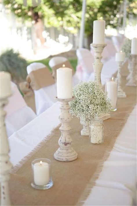 burlap runner over a simple white table cloths and rustic candle holder centerpieces Table Runner With Burlap, Rose Gold White Rustic Dinner Table, Rose Gold White Rustic Table Setting, Ivory And Burlap Table Setting, Rustic Burlap Table Runner, Burlap Runner On Picnic Table, Natyral Blush Western Wedding Table Center, Rustic Wedding Runner Table, Simple Rustic Bride And Groom Table