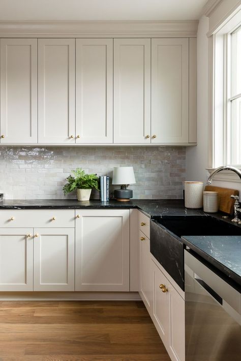 Cream-colored cabinetry with a zellige tile backsplash and black soapstone counters and sink. Brass knobs complete the design. Kitchen Countertops Decor, Kitchen Black Counter, Cream Kitchen Cabinets, Black Kitchen Countertops, Taupe Kitchen, Cream Kitchen, Black Countertops, Kitchen Black, Dry Bar