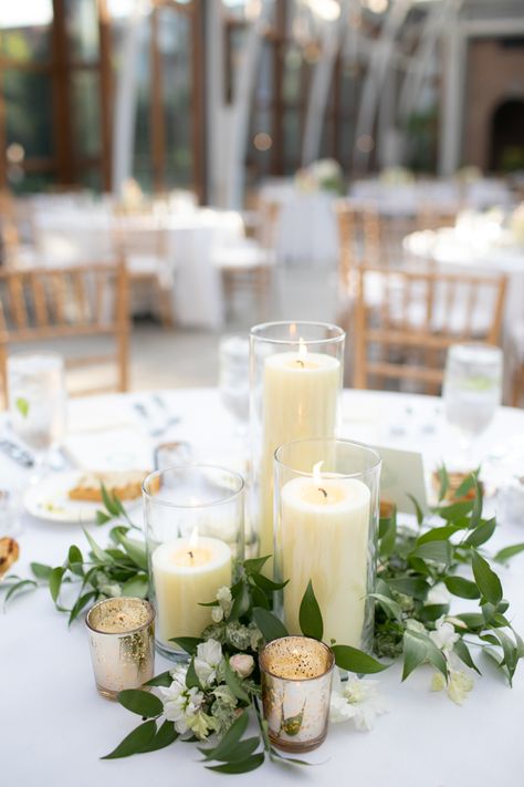 Candle Centerpiece at Romantic Orangerie at Tower Hill Botanic Garden Massachusetts Wedding #weddings #wedding #weddingplanning #weddingflowers #floraldesign Greenery And Candles Centerpieces, Candle Floral Arrangements, Candle With Greenery Centerpiece, Wedding Pillar Candle Centerpieces, Wedding Table Pillar Candles, White Flower Candle Centerpieces, Floral And Candle Centerpiece Wedding Round Table, Round Wedding Tables With Candles, Candles And Greenery Centerpiece Round Table