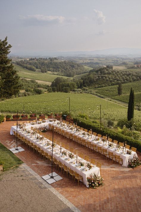 Long dining tables arrange for an outdoor wedding reception in Tuscany, Italy. Rolling hills captured in the backdrop. Long Outdoor Wedding Table, Long Tables For Wedding Reception, Wedding Themes Italy, Outdoor Wedding Long Tables, One Big Wedding Table, Tuscany Wedding Table Decor, Garden Wedding Italy, Italian Vibes Wedding, Italy Wedding Tuscany